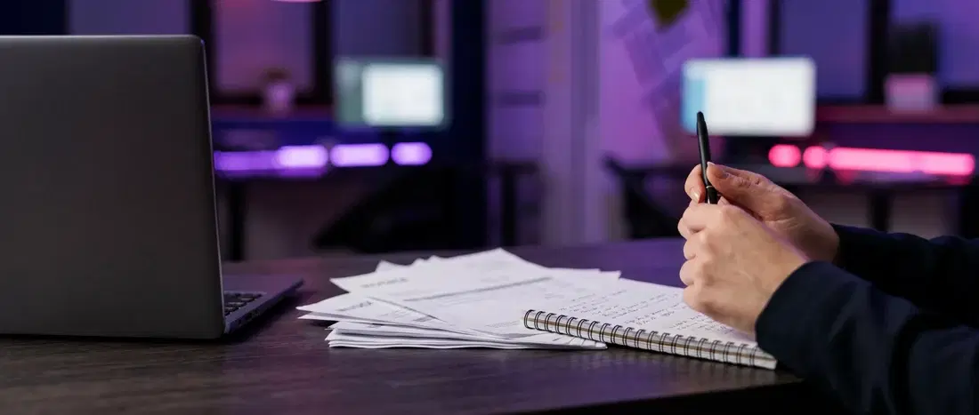 Caderno anotado à mão e laptop, no fechamento do mês da agência