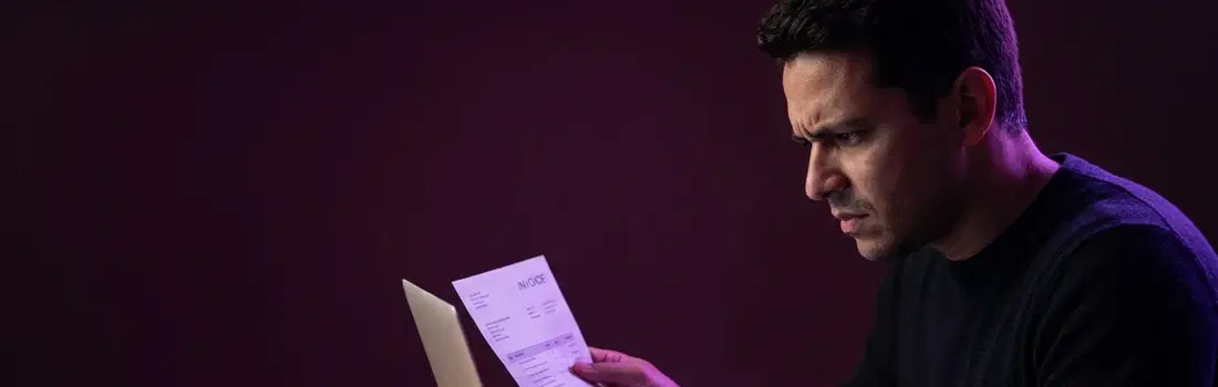 Infoprodutor conferindo uma nota impressa em frente ao laptop